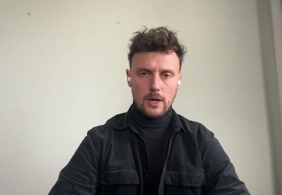 Portret doktora Łukasza Grabarczyka w białym fartuchu lekarskim, w tle nowoczesnego wnętrza szpitalnego.