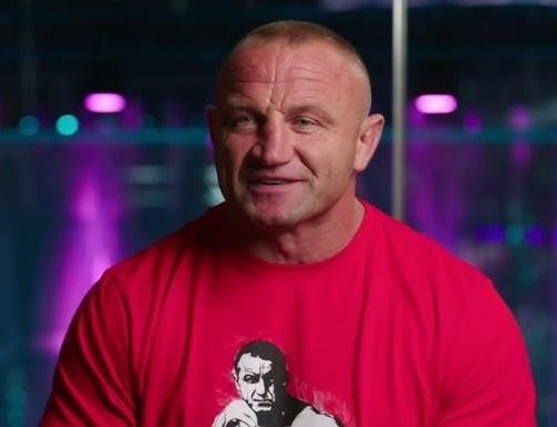 Mariusz Pudzianowski w akcji podczas walki MMA na gali KSW, w dynamicznej pozie zdeterminowanego zawodnika.